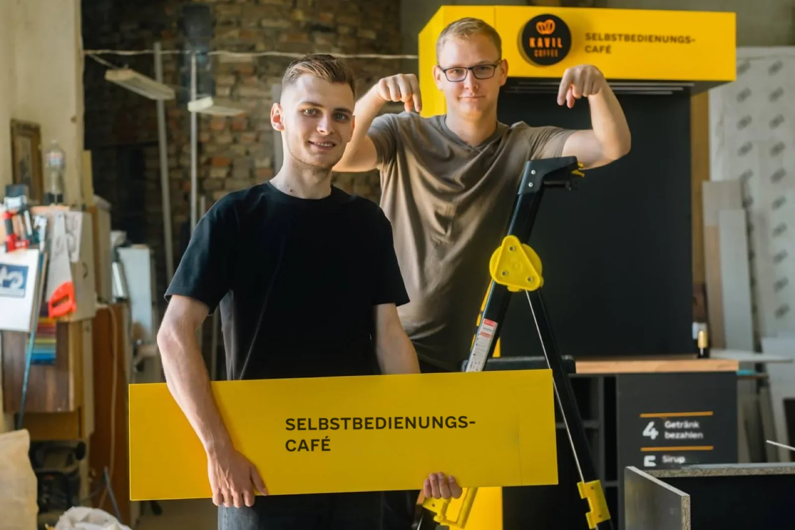 Kavil-Fertigung: Team mit dem Schild „Selbstbedienungs-Café“ neben einem Kiosk im Bau